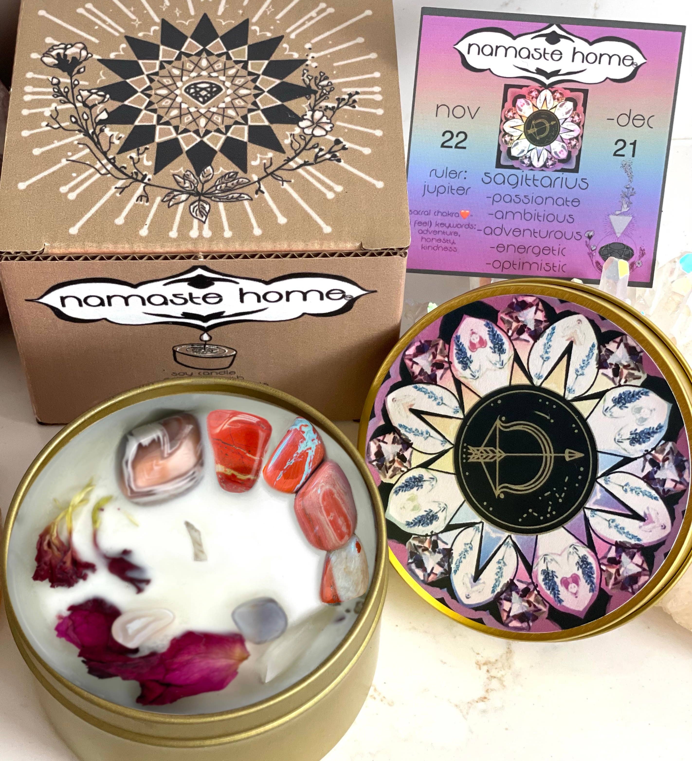 The Sagitarius Crystal Candle opened with the lid to the right of it. The packaging of the Saggitarius Crystal Candle is behind the candle next to a card.
