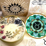The Taurus Crystal Candle opened with the lid to the right of it. The packaging of the Taurus Crystal Candle is behind the candle next to a card.