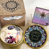The Cancer Crystal Candle opened with the lid to the right of it. The packaging of the Cancer Crystal Candle is behind the candle next to a card.