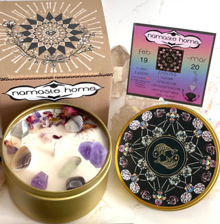 The Pisces Crystal Candle opened with the lid to the right of it. The packaging of the Pisces Crystal Candle is behind the candle next to a card.