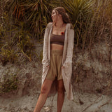 A woman wearing the earthy Sun Ray Cardigan in front of a sand dune at the beach.
