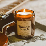 The Thunder Struck candle lit and next to a guitar.