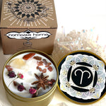 The Aries Crystal Candle opened with the lid to the right of it. The packaging of the Aries Crystal Candle is behind the candle.