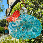 hummingbird feeder blue glass in front of green bushes
