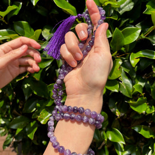model with amethyst mala necklace wrapped around her hand on greenery background