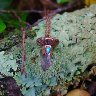 Electroformed amethyst and turquoise mushroom pendant on mossy log in forest