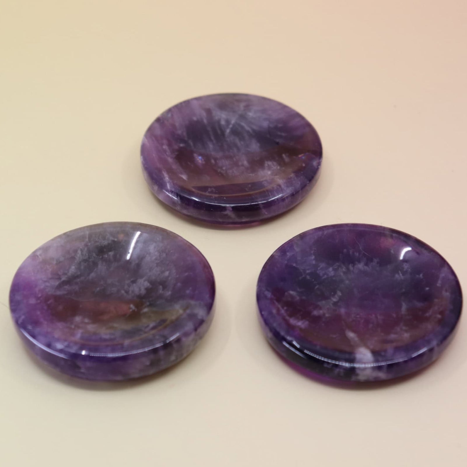 Three purple amethyst crystal stone sphere stands bowls on a beige background