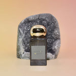 Hippie Water Perfume bottle with gold cap on a gray stone block against a gradient background