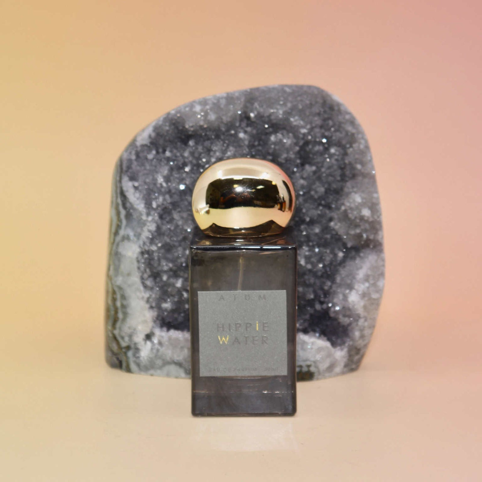 Hippie Water Perfume bottle with gold cap on a gray stone block against a gradient background