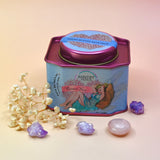 The Coconut Kiss Bath Soak surrounded by crystals and dried flowers on a light pink background.