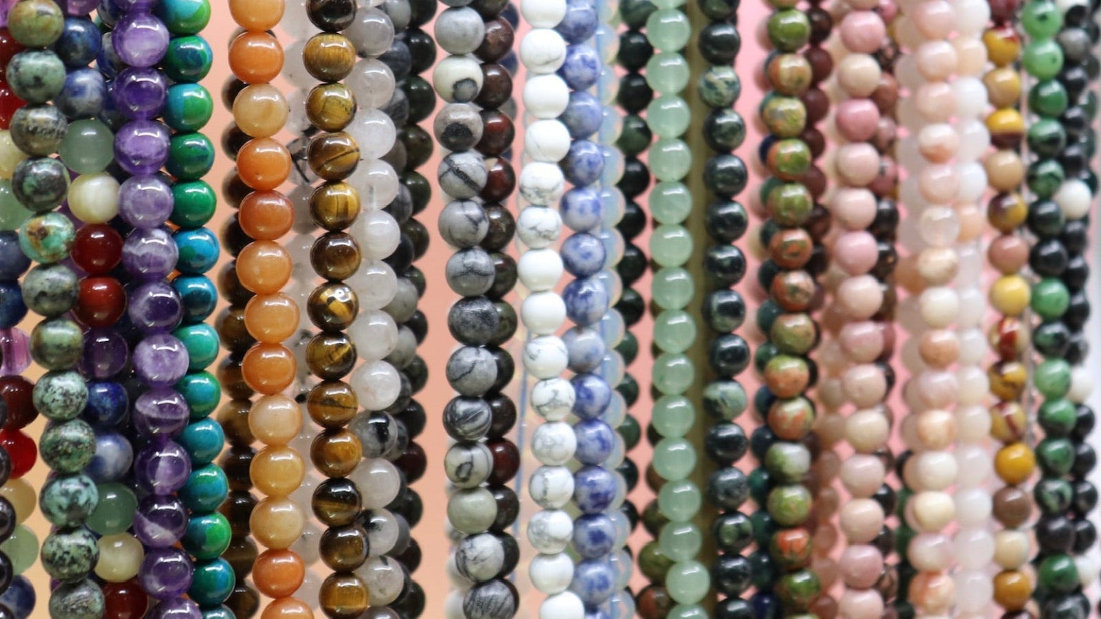 Multiple strands of multicolored beads on a pink background
