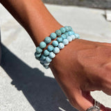 Hand wearing a stack of Larimar beaded bracelets on a blurred background