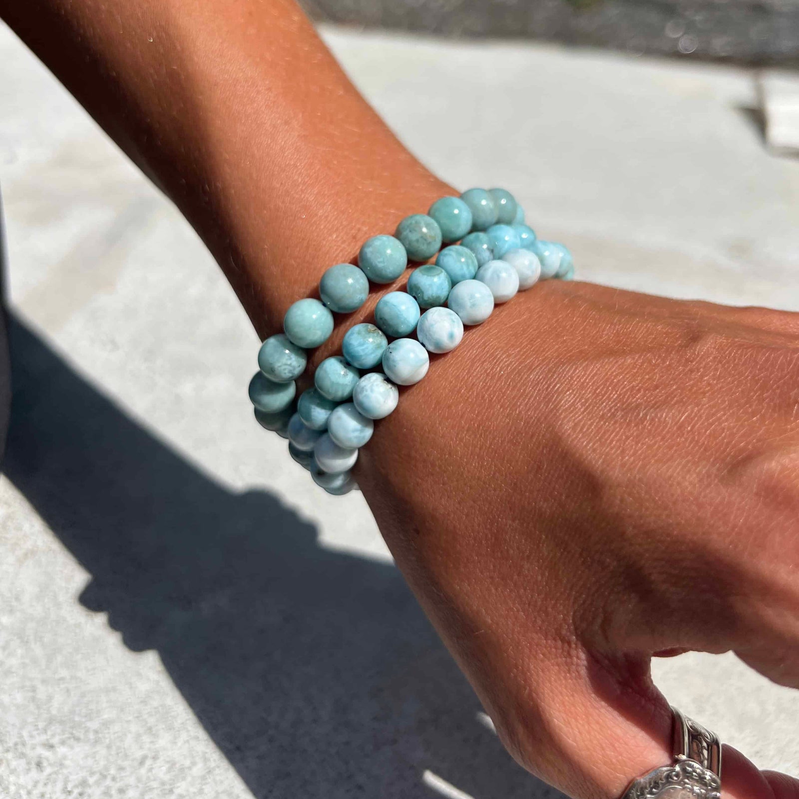 Hand wearing a stack of Larimar beaded bracelets on a blurred background
