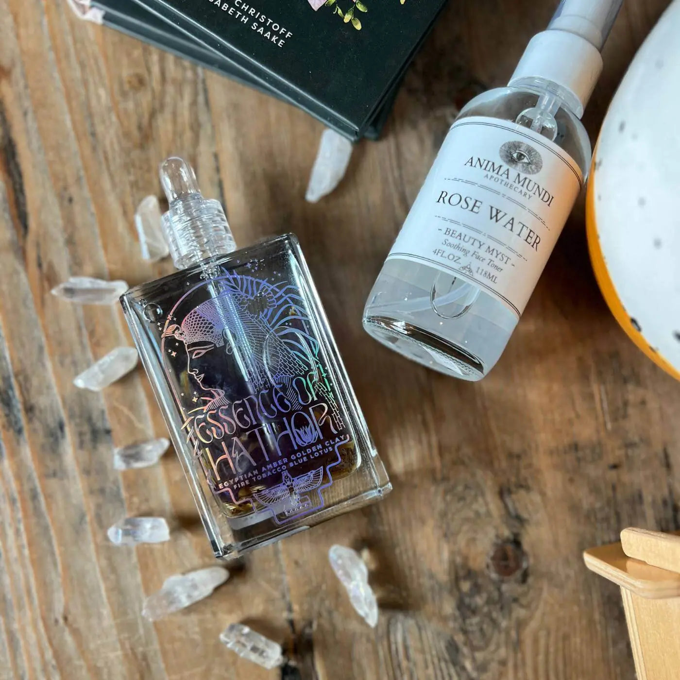 Two bottles on a wooden surface with 'Anima Mundi' rose water bottle and blue lotus oil.