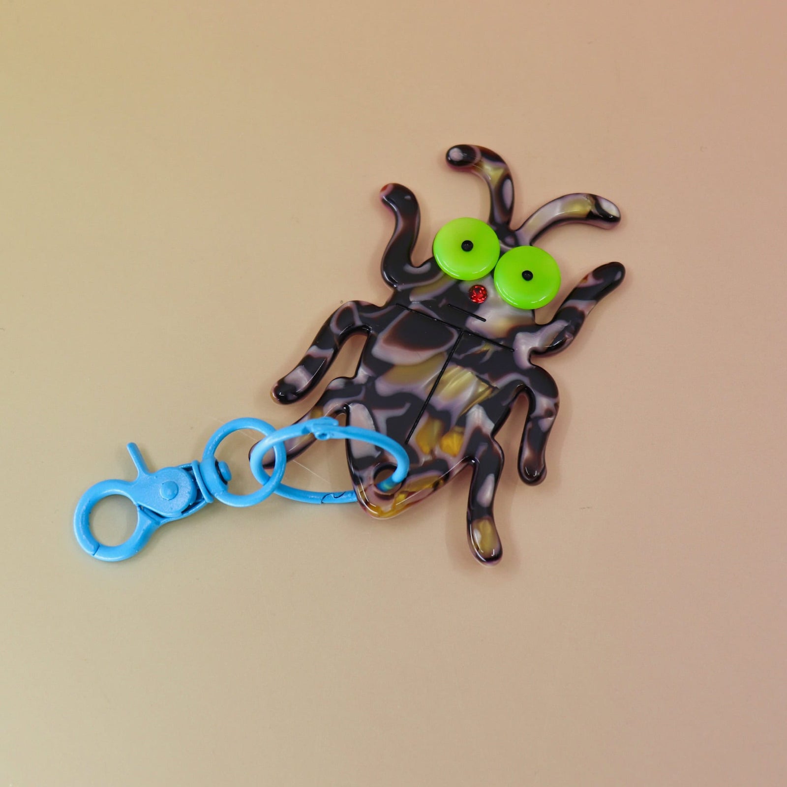 Flat lay of bug keychain with neon eyes and blue clip