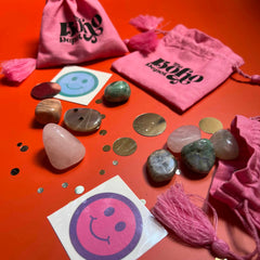 Pink drawstring bags with 'Boho' text, stones, tassels, and smiley face stickers on a red background.