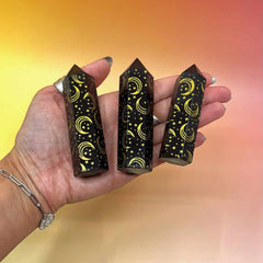 Three black crystal points with star and moon designs held in a hand against a gradient background.