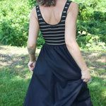 Back view of woman walking away in a striped tank dress with gathered black midi skirt.