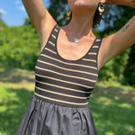 Woman with tattoos standing barefoot in a field wearing a striped ribbed top and long black skirt dress.
