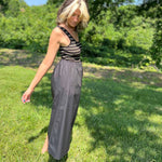 Woman looking down while posing in a black midi dress with striped tank-style top.