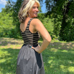Woman standing outdoors, smiling over her shoulder in a sleeveless striped knit and black midi dress.