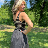 Woman standing outdoors, smiling over her shoulder in a sleeveless striped knit and black midi dress.