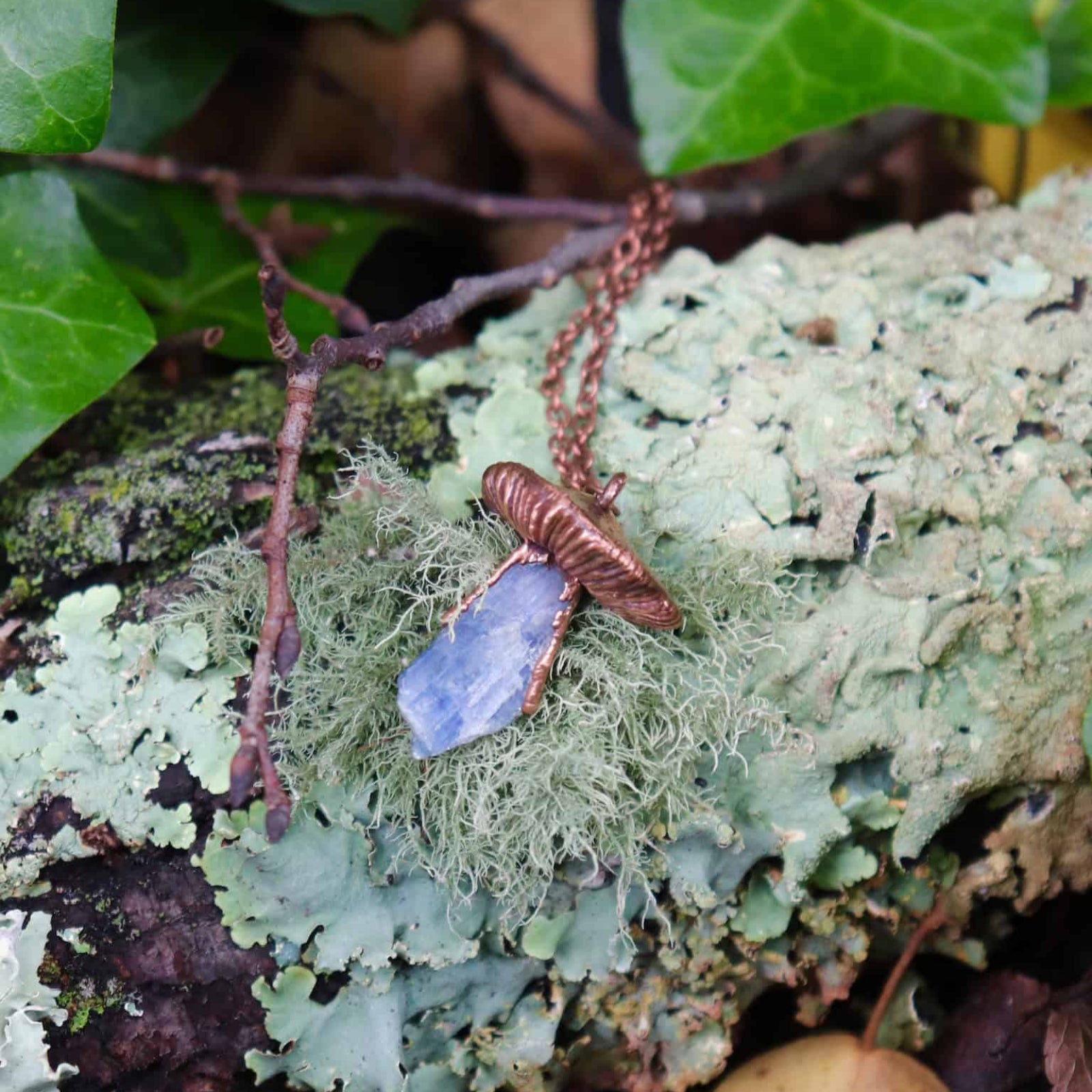 Blue Kyanite mushroom pendant on forest floor with moss and lichen