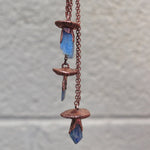Unique copper mushroom necklaces hanging against neutral wall background