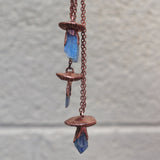 Unique copper mushroom necklaces hanging against neutral wall background