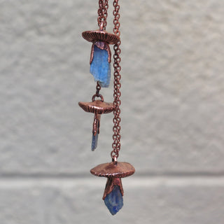 Unique copper mushroom necklaces hanging against neutral wall background
