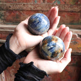 Two hands holding two marbled stone spheres against a textured wall.