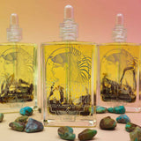 3 bottles standing up of essence of hathor blue lotus oil on a pink and orange pastel background with turquoise stones scattered in front