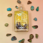 Essence of Hathor oil glass bottle laid flat on orange and pink pastel background with turquoise stones around in a circle