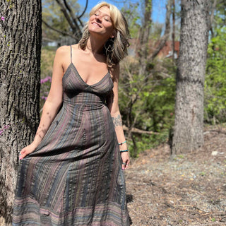 model wearing striped sundress with head up towards the sun smiling in front of trees