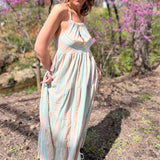 model wearing teal striped sundress looking down at ground in front of pink trees