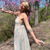 side view of teal striped sundress on model who has arms stretched out in glee and smiling in front of pink trees and forest