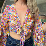 A woman wearing the rainbow Hippie Bohemian Bell Sleeve Wrap Top with black pants in front of a rusted vintage Volkswagen bus.