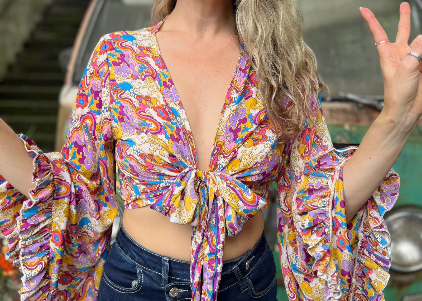 A woman wearing the rainbow Hippie Bohemian Bell Sleeve Wrap Top with black pants in front of a rusted vintage Volkswagen bus.