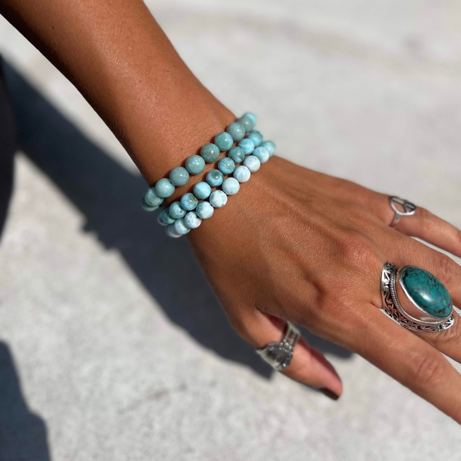 Hand wearing multiple Larimar beaded bracelets on a light background