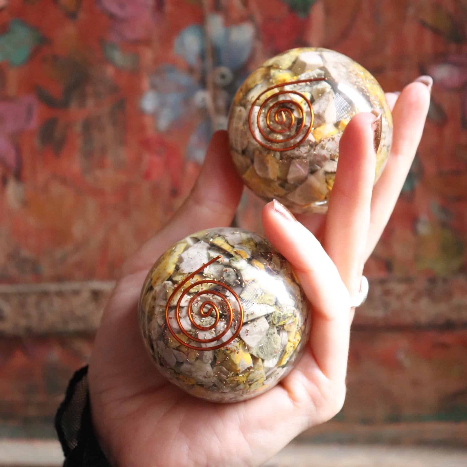Two crystal balls with spiral designs held by a hand against a colorful floral background