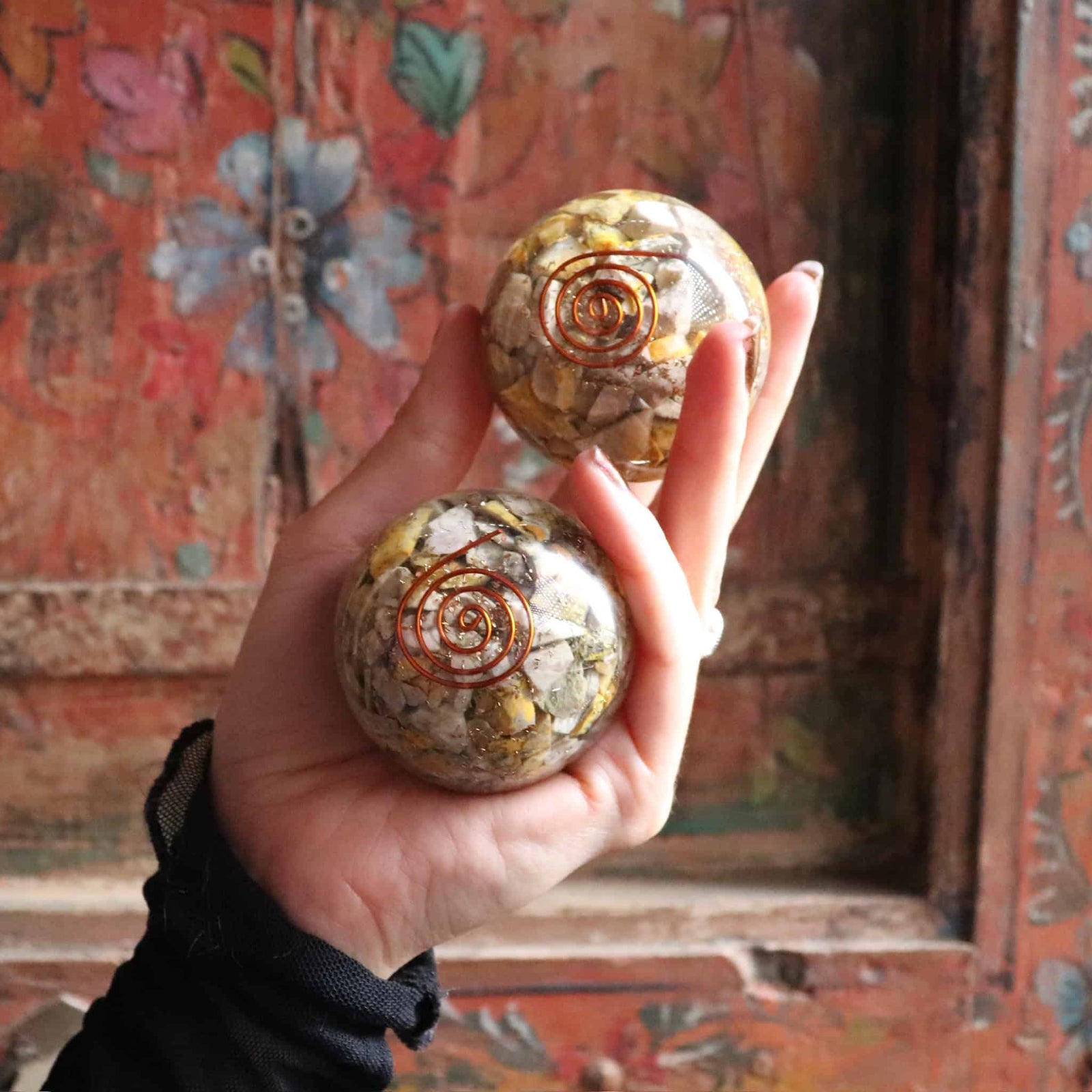 Hand holding two crystal balls with spiral patterns against a decorative background