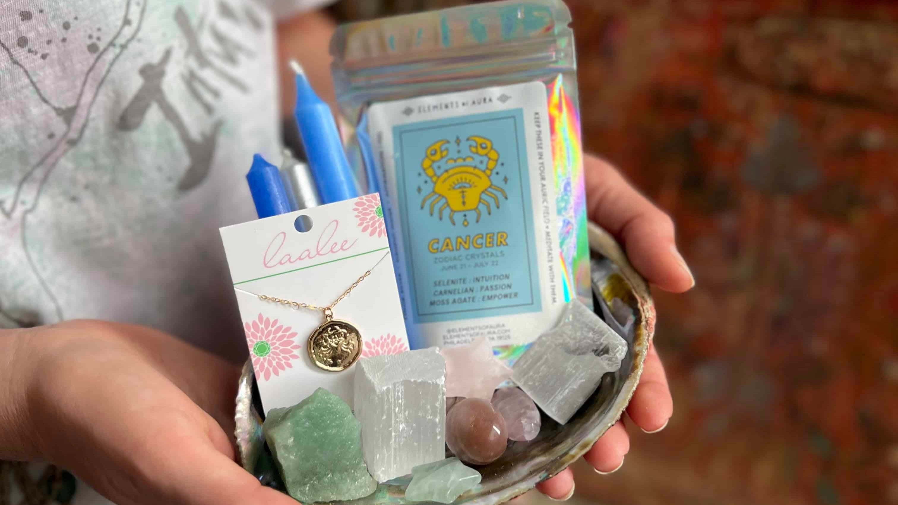 Person holding a small dish with items including a necklace, cards, and stones.