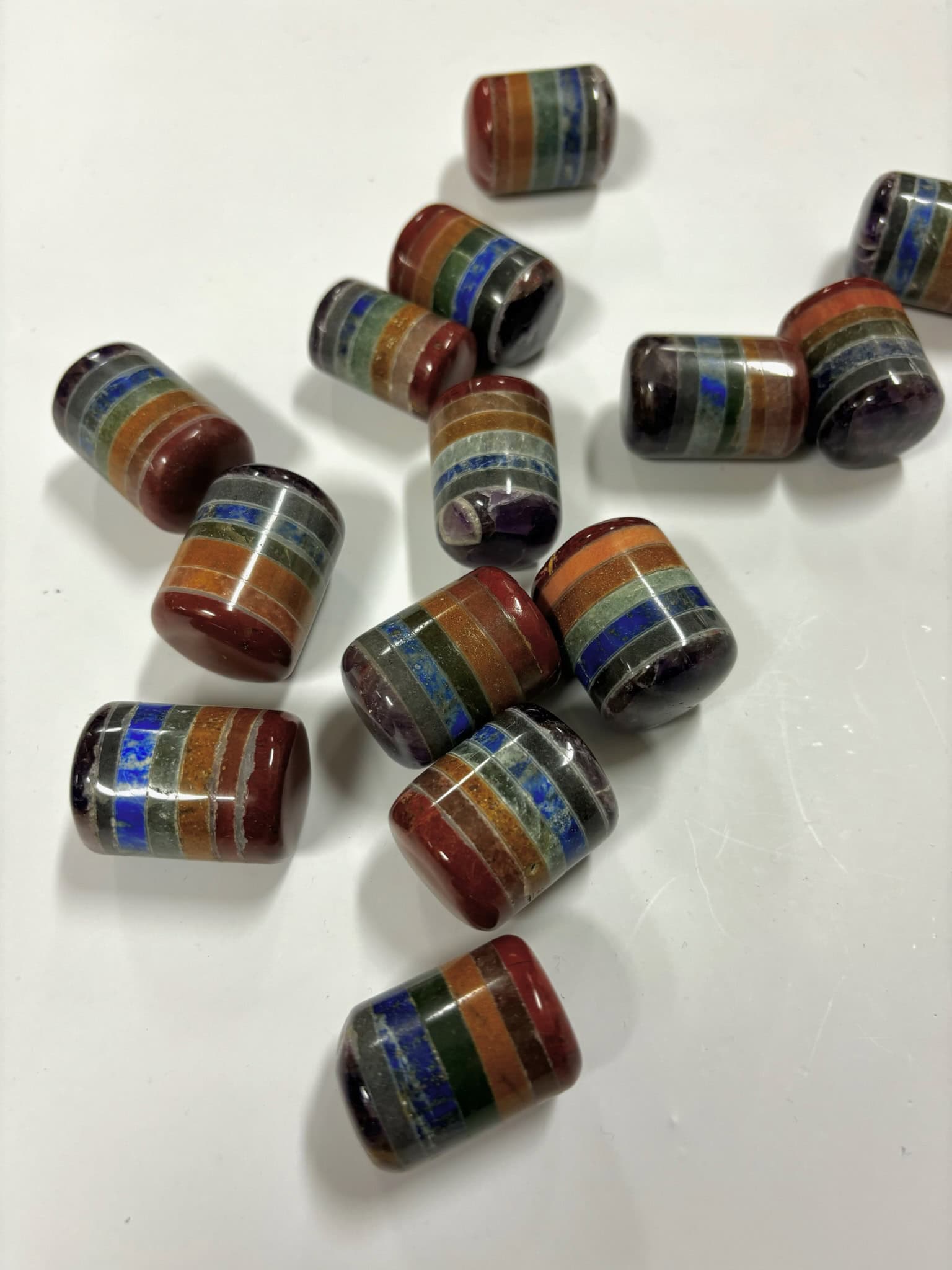 Multiple layered chakra cylinder tumbled stones on a white background, each featuring stacked colorful crystal layers