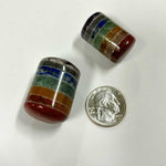 Two chakra cylinder tumbles next to a U.S. quarter to show size, featuring vibrant stacked layers of red, orange, green, blue, and purple stones
