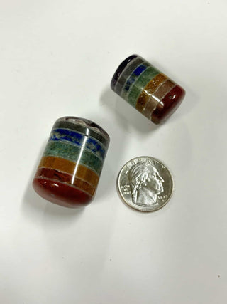 Two chakra cylinder tumbles next to a U.S. quarter to show size, featuring vibrant stacked layers of red, orange, green, blue, and purple stones