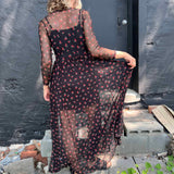 Back view of a woman wearing a black mesh cherry print maxi dress, showing the sheer detail and attached slip.