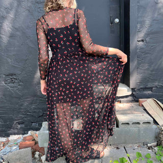Back view of a woman wearing a black mesh cherry print maxi dress, showing the sheer detail and attached slip.
