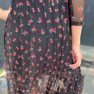 Back view of a woman wearing a black mesh cherry print maxi dress, showing the sheer detail and attached slip close up view