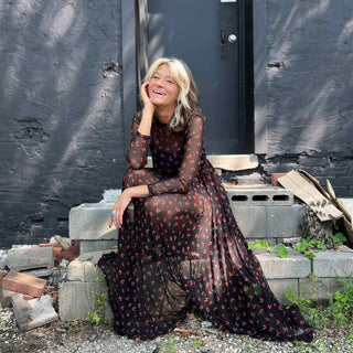 Woman seated in a cherry print mesh dress, gazing directly ahead with a smile expression.