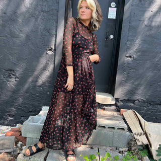 Woman swaying in a flowy cherry print maxi dress with sheer sleeves and mock neck.